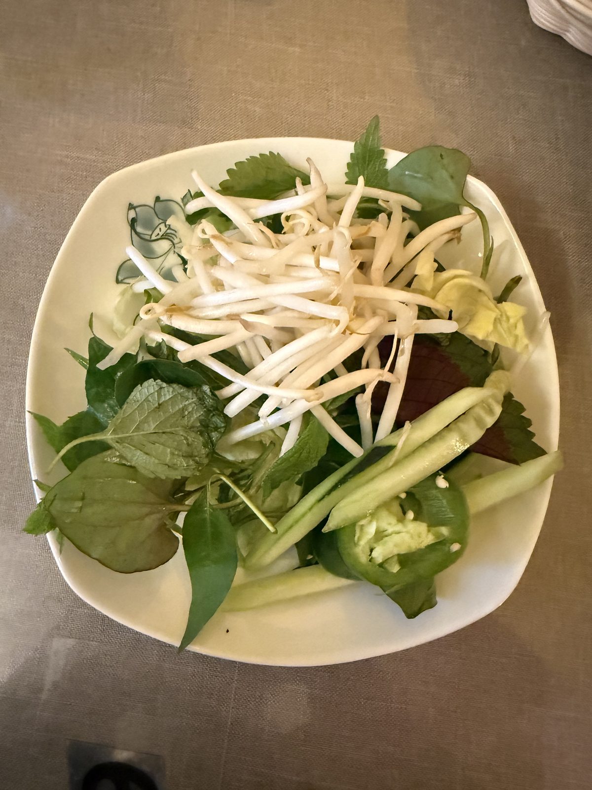 The herb plate — bean sprouts, Thai basil, perilla, cucumber, and enough jalapeño to matter.