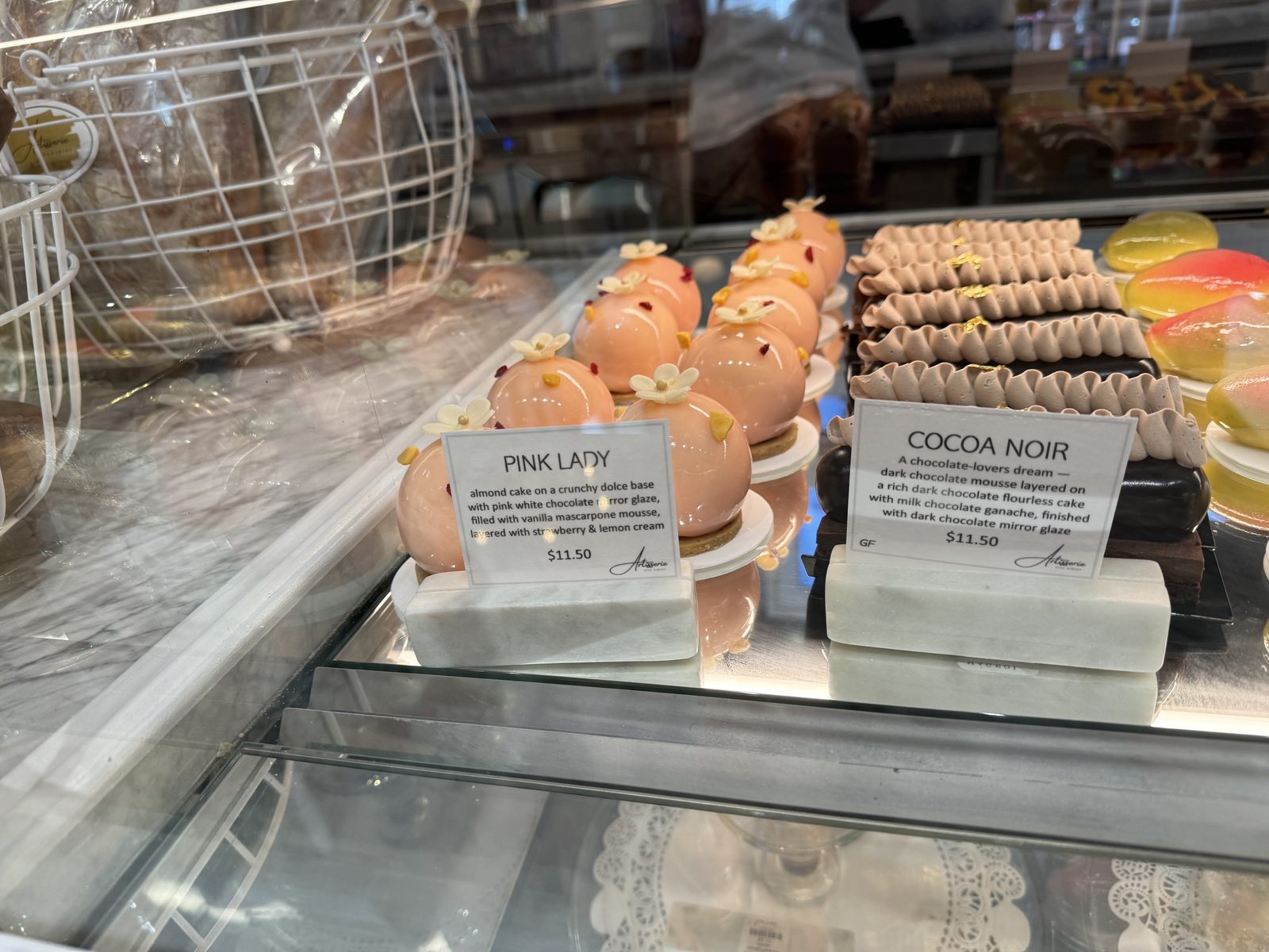 The case, mid-morning. Pink Lady on the left, Cocoa Noir — a dark-chocolate entremet — on the right for scale.
