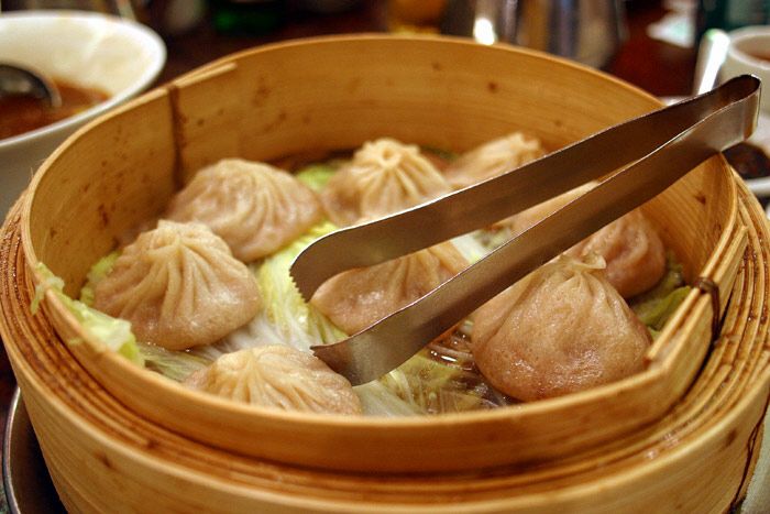 Xiao long bao in a bamboo steamer, the pleated tops and thin skins typical of the style