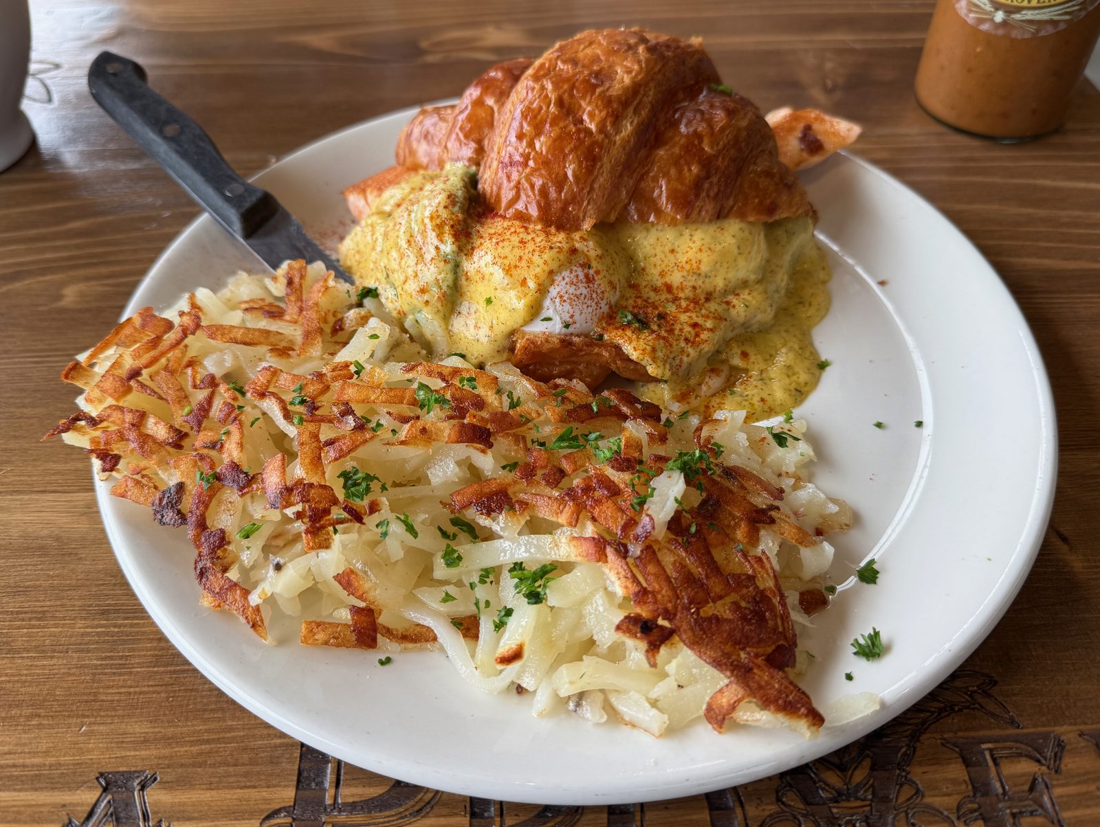 The salmon Benedict, on a table carved with the restaurant's own name. That is the corner of the sauce bottle at the top right — we will get to the bottle.