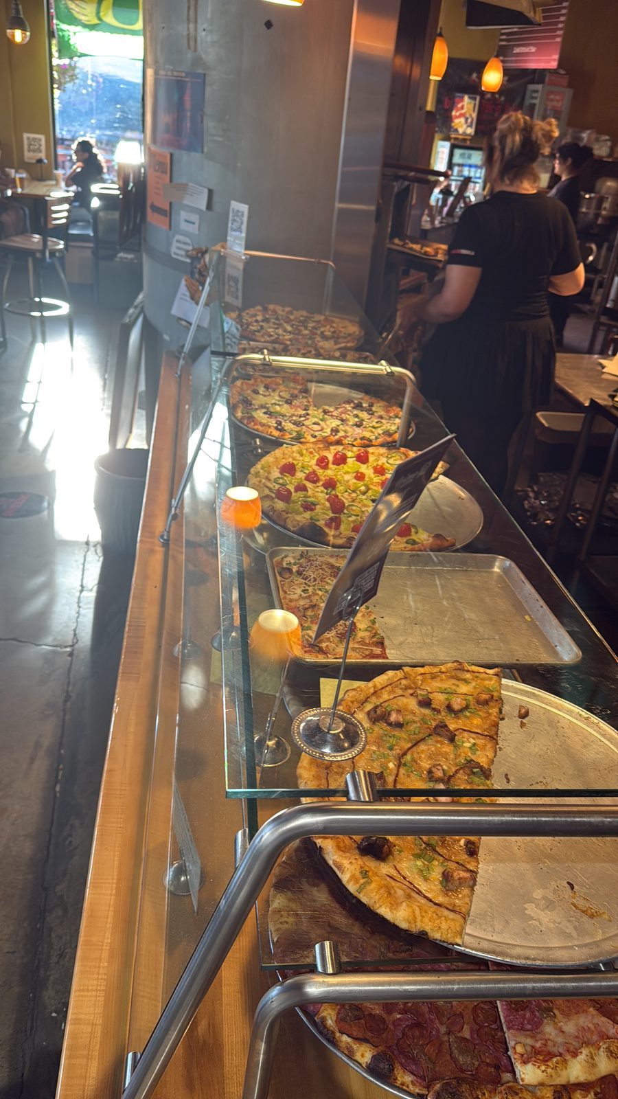 The case, mid-afternoon rush. Whole pies under glass, each one labeled by hand.